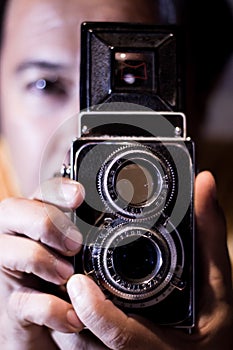 Man with old vintage camera in hands. Focus to man eyes. Vintage stylized photo of man photographer with old TLR Twin Lens Reflex