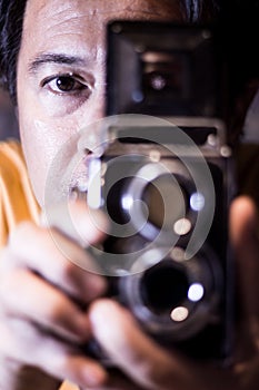 Man with old vintage camera in hands. Focus to man eyes. Vintage stylized photo of man photographer with old TLR Twin Lens Reflex