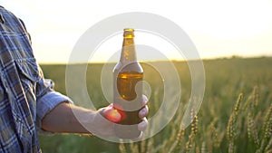 Man open a bottle of beer on background of the ripe wheat field at sunset. A man`s hand opens a bottle of beer. Sun lens