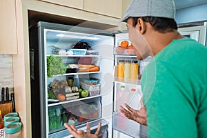 man open fridge door and confuse looking something to eat