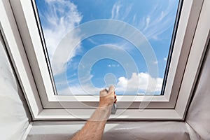 Man open new skylight mansard window in an attic room against blue sky.