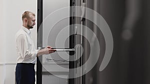 Man open server rack and typing at laptop in datacenter room