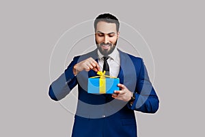 Man opening gift box, unwrapping present for celebrating holiday, pulling ribbon, looking at gift.