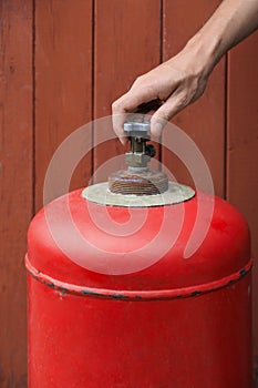 Man opening red gas cylinder near brown wooden wall, closeup