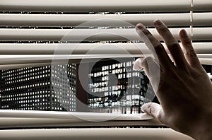 Man opening window blinds seeing business towers