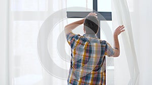 Man opening window curtain raising arms at home