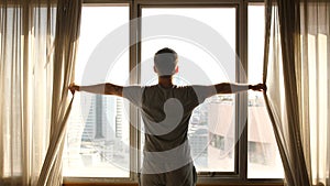 Man Opening the Window Curtain on a Sunny Morning in a Hotel Room, a Man Looking on the Window Relaxed.