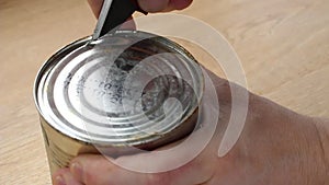 A man opens a can of food with a knife.