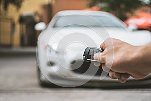 The man opens the car with a keychain, in the background is a white car