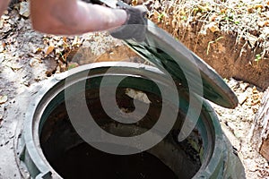 The man opens a sewer hatch. Septic tank inspection and maintenance