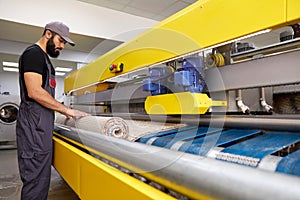 Man operating carpet automatic washing machine in professional laundry service