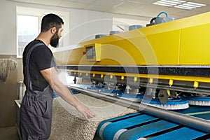 Man operating carpet automatic washing machine in professional laundry service