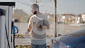 Man operating an electric car charging station while using phone