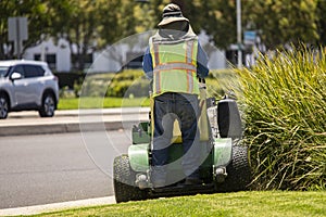 A man operating a large standup lawnmower wearing a safety vest