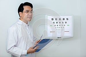 Man ophthalmologist wear uniform holding clipboard standing near eye chart vision test in clinic