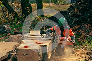 A man in an orange jacket cuts boards with an alaskan portable chainsaw mill.