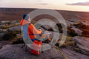 Man in orange jacket relaxing alone on the top of  mountain  and drinking hot coffee at sunrise. Travel  Lifestyle