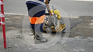 Man in an orange protective uniform tamps a freshly laid asphalt pavement