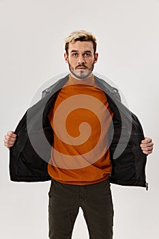 man in orange sweater and unbuttoned jacket on a light background blond portrait cropped view