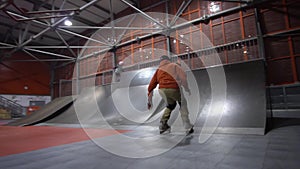 A man in an orange sweatshirt goes rollerblading in an extreme park, slow motion. Kobayashi