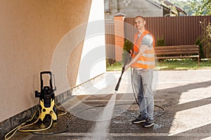A man in an orange vest cleans a tile of grass in his yard near the house. High pressure cleaning