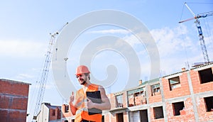 Man orange vest and helmet works at construction site. Contractor control according to plan. Control construction