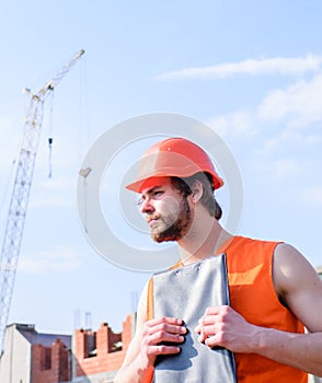 Man orange vest and helmet works at construction site. Contractor control according to plan. Guy in protective helmet