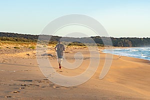 Man out for an early morning run on the beach orange sand saphire blue sea early morning light