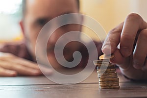 Man out of focus stacking coins on top of a wooden table