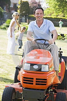 Man outdoors driving lawnmower smiling with family