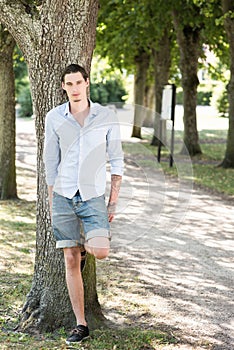 Man outdoors leaning on a tree