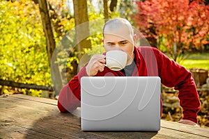 Man outdoors looking at Laptop and Drinking Coffee