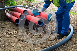A man in overalls and a bright vest closes large red plastic pipes with blue caps