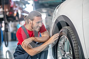 Man in overalls crouched near car wheel