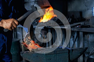 Man in overalls forging molten metal on anvil