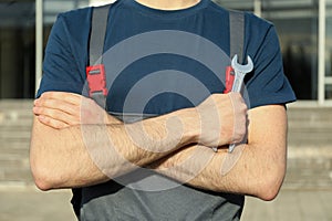 Man in overalls holding wrench with folded arms. Car inspection