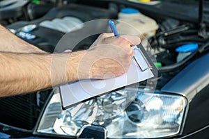 A man in overalls writes to clipboard. Mechanic. Car inspection