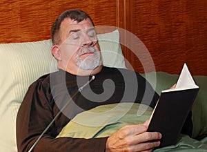 Man with Oxygen Cannula Reading in Bed photo