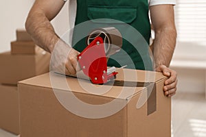 Man packing box with adhesive tape indoors. Moving service