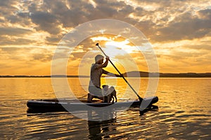 Man paddle boarding at lake during sunset together with pug dog. Concept of active tourism with pets