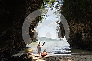 Man with a paddle standing next to sea kayak at secluded beach in Krabi, Thailand