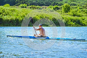 Man paddling a blue and yellow kayak on the river near the shore. Kayaking concept.A man swims in a canoe on the river. A man in a