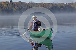 Man Paddling a Canoe with a Small White Dog in the Bow