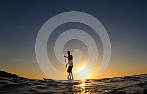 Hombre remando su surfear lámina sobre el atardecer 