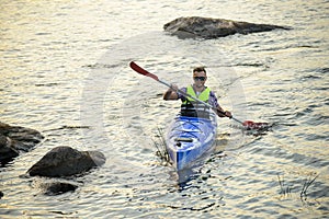 Man Paddling Kayak on Beautiful River or Lake among Stones at the Evening