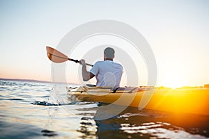 Man paddling the kayak at sunset