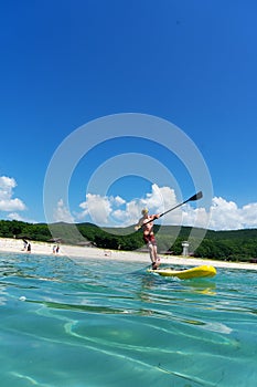 Man is paddling on a yellow SUP board on a sea waves at sunny day.