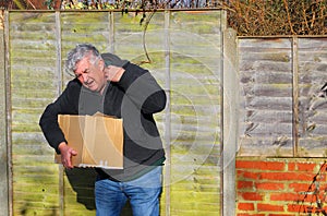 Man in pain carrying heavy box. Shoulder strain.