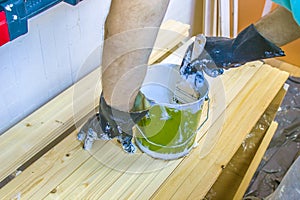 Man with paintbrush in hand and painting on the wooden board with white paint. Metal bucket with white paint, lining