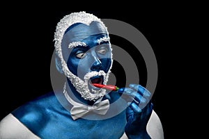 Man painted in blue color with snowy hair and beard eating chili pepper